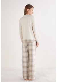 Top de manga larga color beige claro con escote redondeado, combinado con pantalones holgados de cuadros en tonos beige y azul, confeccionados con tela suave.