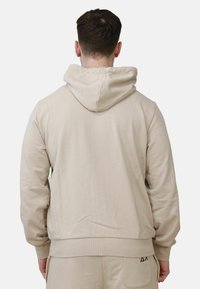 Felpa beige con cappuccio e polsini a costine. Presenta una texture liscia e un piccolo logo vicino all'orlo. Design casual e vestibilità rilassata.