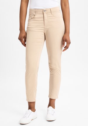 Beige aansluitende broek met een gladde textuur, vijf-pocket ontwerp en een ritsluiting. Draag met witte sneakers met ronde neuzen en veters.