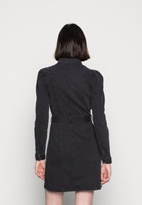 Robe en denim noir avec un col, manches longues, taille cintrée avec une ceinture et des détails de coutures verticales.