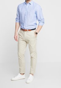 Chemise boutonnée bleu clair aux manches retroussées, chinos beiges et baskets blanches. Ceinture marron. Coupe décontractée avec des lignes épurées et un minimum de détails.