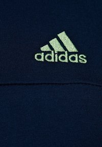 Marinblå atletisk klädsel med ribbad textur. Har en ljusgrön, broderad Adidas-logotyp och tre ränder.