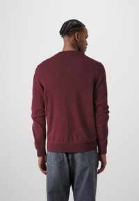Burgundy kötött pulóver kerek nyakkal, bordás mandzsettével és szegéllyel. Szürke farmerrel viselve, zsebekkel, laza szabással.