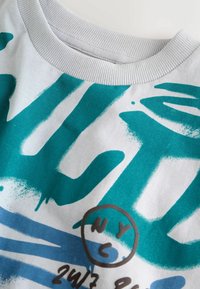 T-shirt bianca con design astratti turchesi e testo, colletto a coste e un logo circolare con accenti "NYC" e "24/7".