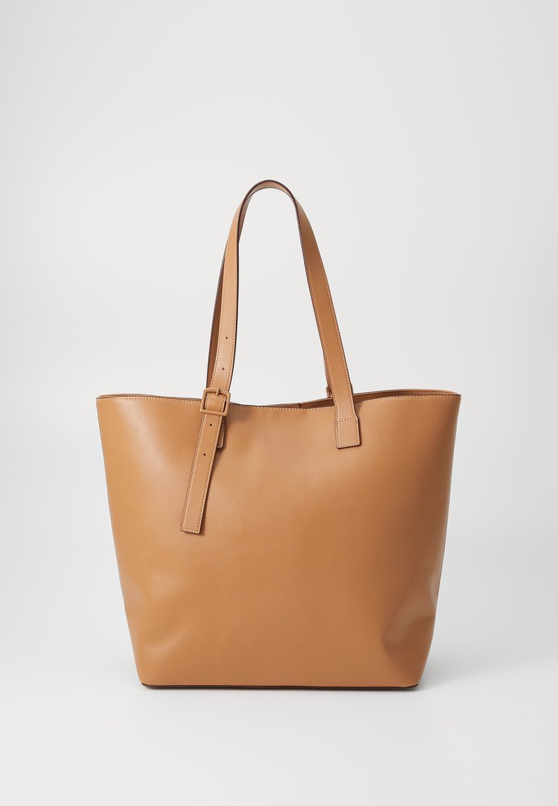 Sac en cuir tan avec des sangles d'épaule réglables, texture lisse et design minimaliste sans embellissements extérieurs.