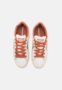 Białe trampki z pomarańczowymi sznurówkami i akcentami, z perforowanymi detalami oraz logo "Converse All Star" na języku.
