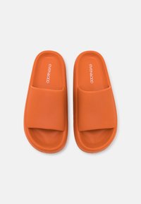 Sandales orange à enfiler avec une surface texturée et une large sangle. Logo imprimé sur le dessus. Matériau léger, design de semelle plate.