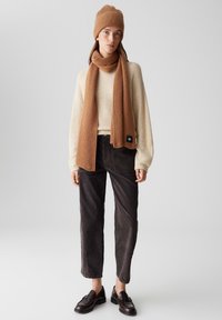 Beanie e sciarpa a coste marroni, maglione fuzzy crema, pantaloni in corduroy scuri, mocassini marroni, design minimalista. Outfit casual a strati.