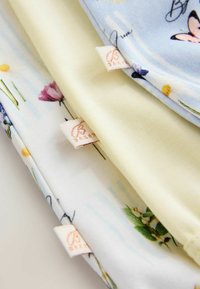 Tessuti morbidi impilati con stampe floreali e di farfalle e piccoli marchi cuciti, su una superficie chiara.