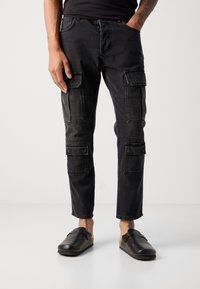 Pantaloni cargo neri con più tasche laterali, una vestibilità rilassata e una leggera trama sbiadita, abbinati a scarpe nere slip-on.
