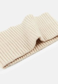 Ribbade stickade pannband i ljusbeige, med en mjuk textur och vikbar design. Materialet verkar elastiskt och bekvämt att bära.