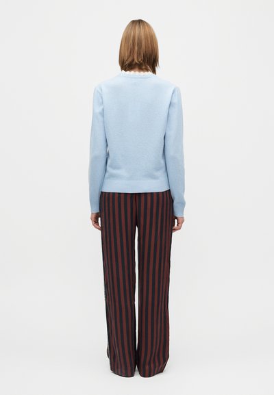 Hellblauer Strickpullover mit rundem Ausschnitt, kombiniert mit hoch taillierter Hose mit vertikalen roten und schwarzen Streifen.