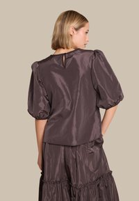 Brun satinkjole med puffede ærmer, har en knap-nøglehul bagpå. Stylet med en matchende ruffleskørt i lagdelt design.