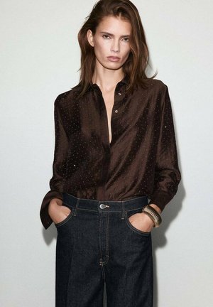 Chemise en soie marron avec un motif à pois subtil, dotée d'un col boutonné et de manches longues, associée à un jean en denim sombre taille haute.