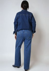 Denim overhemd en wijde jeans in donkerblauw, met een klassieke kraag, knoopmanchetten en subtiele stikdetails op de achterzakken.