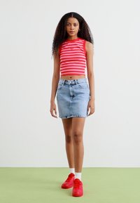 Piros és fehér csíkos crop top könnyű kék farmer szoknyával párosítva. A modell piros sportcipőt visel fehér zoknival. Egyszerű, laza stílus.
