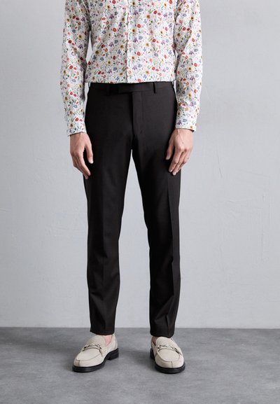 Black tailored trousers with a smooth texture, paired with a colorful floral button-up shirt. Shoes are light beige with a decorative chain.