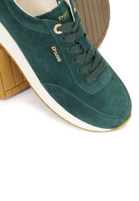 Green suede sneaker with a white midsole and beige rubber outsole, featuring gold logo accents and matching laces. Round toe design.