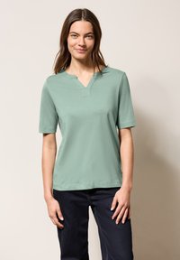 T-shirt a maniche corte e scollatura a V in cotone verde chiaro. Presenta una vestibilità morbida con una texture liscia e dettagli di cucitura minimi.