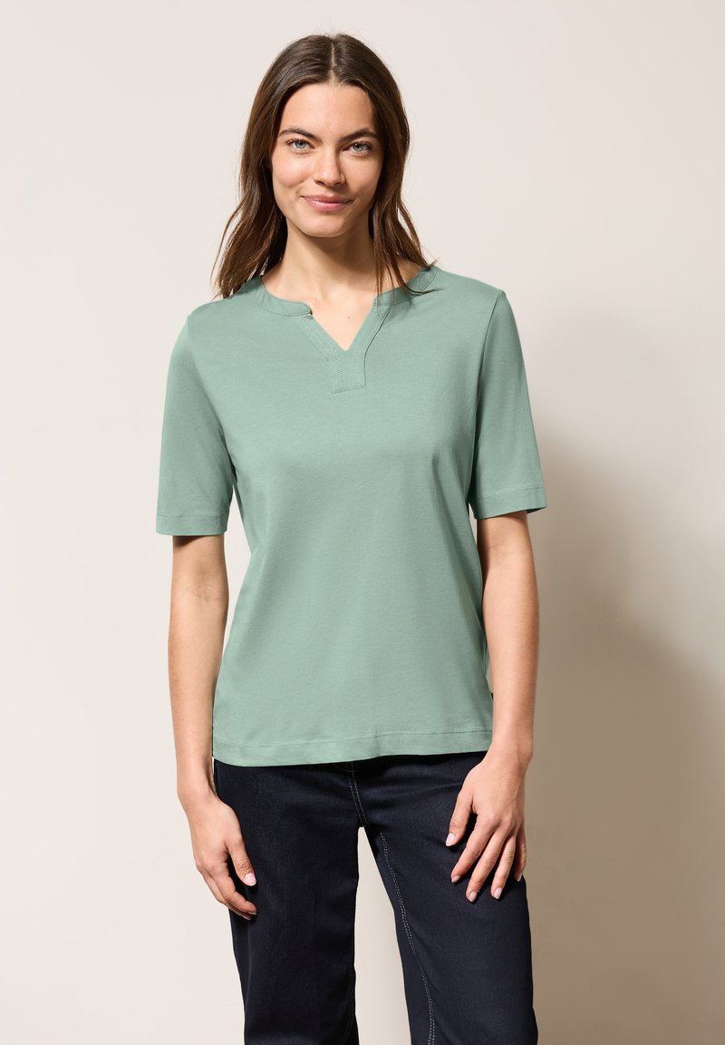 T-shirt a maniche corte e scollatura a V in cotone verde chiaro. Presenta una vestibilità morbida con una texture liscia e dettagli di cucitura minimi.
