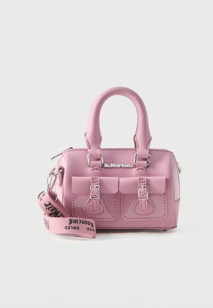 Klein roze Dr. Martens handtasje met twee gespzakken aan de voorkant, afgeronde handvatten en een afneembare stoffen band met merknaam die er voor ligt.