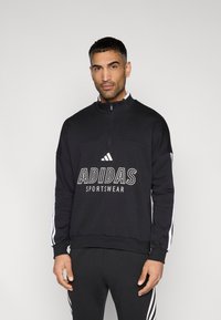 Μαύρο φούτερ adidas με μισό φερμουάρ, λευκό λογότυπο και λευκές πλαϊνές ρίγες. Διαθέτει μακριά μανίκια και ριμπ μανσέτες.