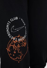 Sudadera negra con gráficos naranjas de un globo terráqueo y una estrella fugaz, con el texto "ASTRONOMY CLUB - NIKE SPORTSWEAR."