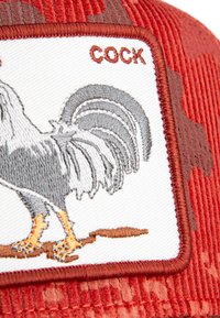 Tissu en velours côtelé rouge avec un patch brodé représentant un coq gris se tenant sur une branche, avec le mot "COQ" brodé au-dessus.