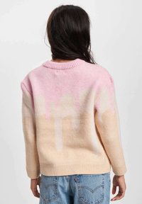 Strikkegenser med en rosa og beige gradient, med ribbestrikket halslinning og avrundet kant. Myk tekstur, nedfalne skuldre, og fargeblokkdesign.