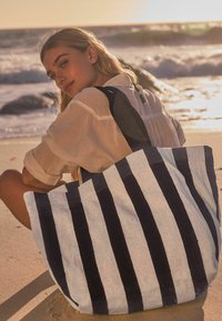 Grote gestreepte tote bag van zacht materiaal, met afwisselende marineblauwe en lichtgrijze strepen, en brede handvatten voor eenvoudig dragen.