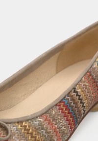 Μοντέρνο παπούτσι με φλατ σόλα και περιμετρικά μπεζ μοκέτα σουέντ. Το επάνω μέρος παρουσιάζει υφαντό πολύχρωμο ζιγκ ζαγκ μοτίβο. Εσωτερικό σε ανοιχτό μπεζ και χαμηλό τακούνι.