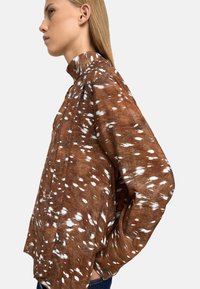 Brązowa, teksturowana bluzka z białymi plamkami, wysoki kołnierz i luźne rękawy. Wykonana z miękkiego materiału, charakteryzuje się swobodnym krojem.