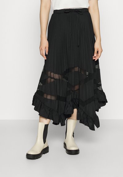 Jupe midi plissée noire avec des panneaux transparents, un ourlet à volants et une taille ajustable avec cordon. Associée à des bottines beige et des accents noirs.