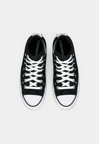 Adidași negri din pânză, cu șireturi albe, vârfuri din cauciuc și știfturi argintii pe laterale. Talpa din cauciuc alb și logo-ul mărcii imprimat vizibil.