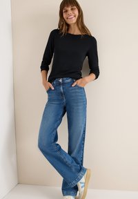 Zwarte lange mouwen top gecombineerd met lichtblauwe recht gesneden jeans. Beschikt over zakken, klassieke denimtextuur en lichte slijtage aan de zoom.