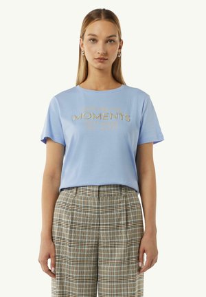 T-shirt en coton bleu clair à manches courtes, avec un texte doré brodé "Capturez les moments qui vous rendent heureux." Associé à un pantalon à carreaux.