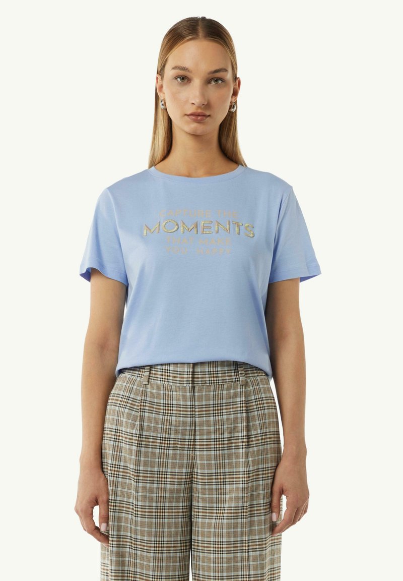 T-shirt en coton bleu clair à manches courtes, avec un texte doré brodé "Capturez les moments qui vous rendent heureux." Associé à un pantalon à carreaux.