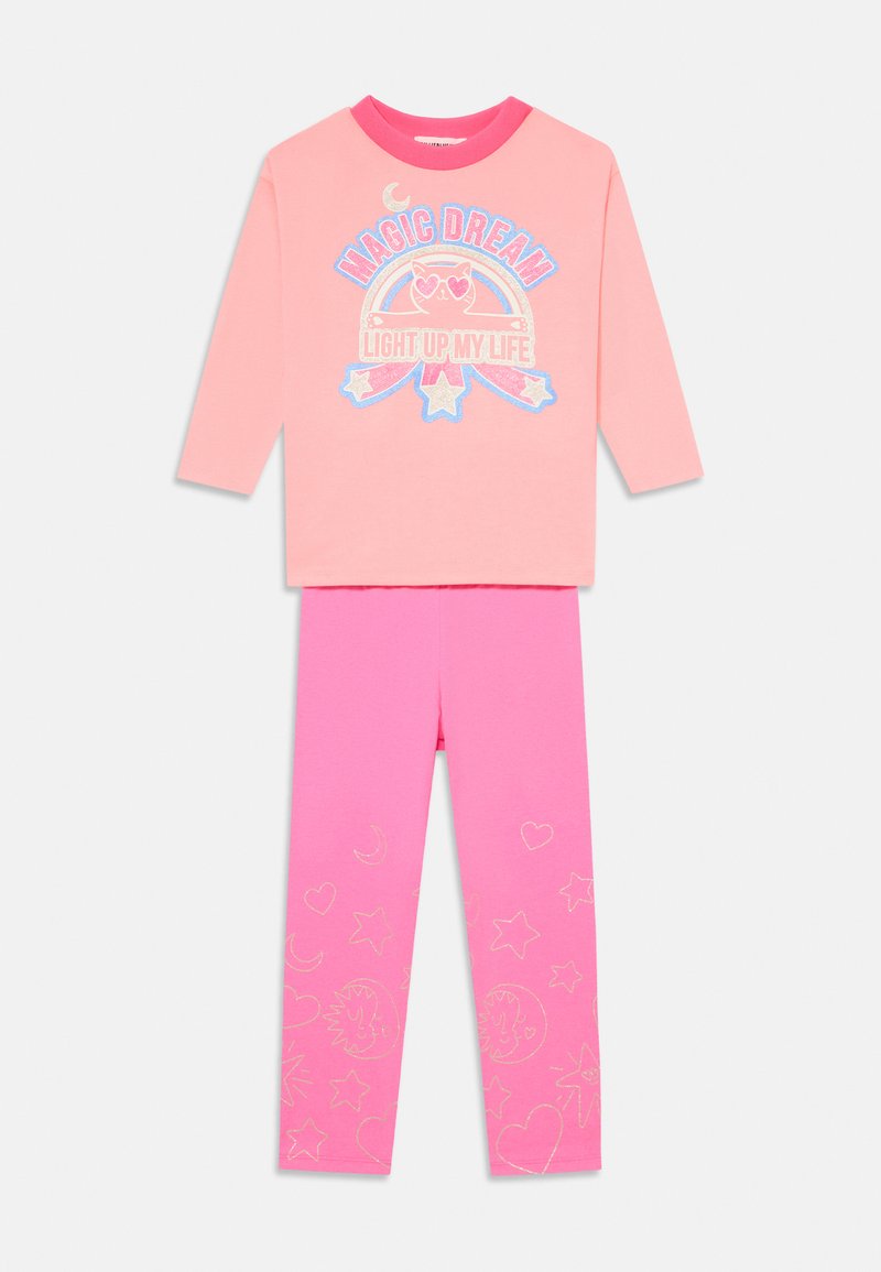 Vaaleanpunainen pitkähihainen toppi, jossa on teksti "Taianomainen unelma valaisee elämäni" ja sarjakuvamainen kissakuva. Yhdistetty kirkkaanpunaisten legginsien kanssa, joita koristavat tähdet ja sydämet.