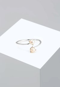 Bague en argent ornée de deux perles rose pâle, montées sur des bandes délicates et courbées, créant un design minimaliste et élégant.