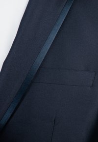 Tissu de veste de costume bleu marine avec une texture lisse, dotée d'un cordon en satin le long du revers et d'une poche latérale.