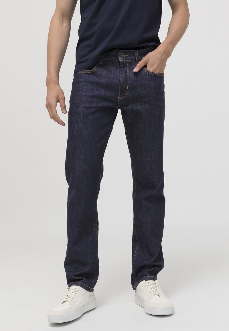 Donkerblauwe denim jeans met een rechte pasvorm, subtiele textuur, contrasterende stiksels en voorzakken, gecombineerd met witte sneakers.