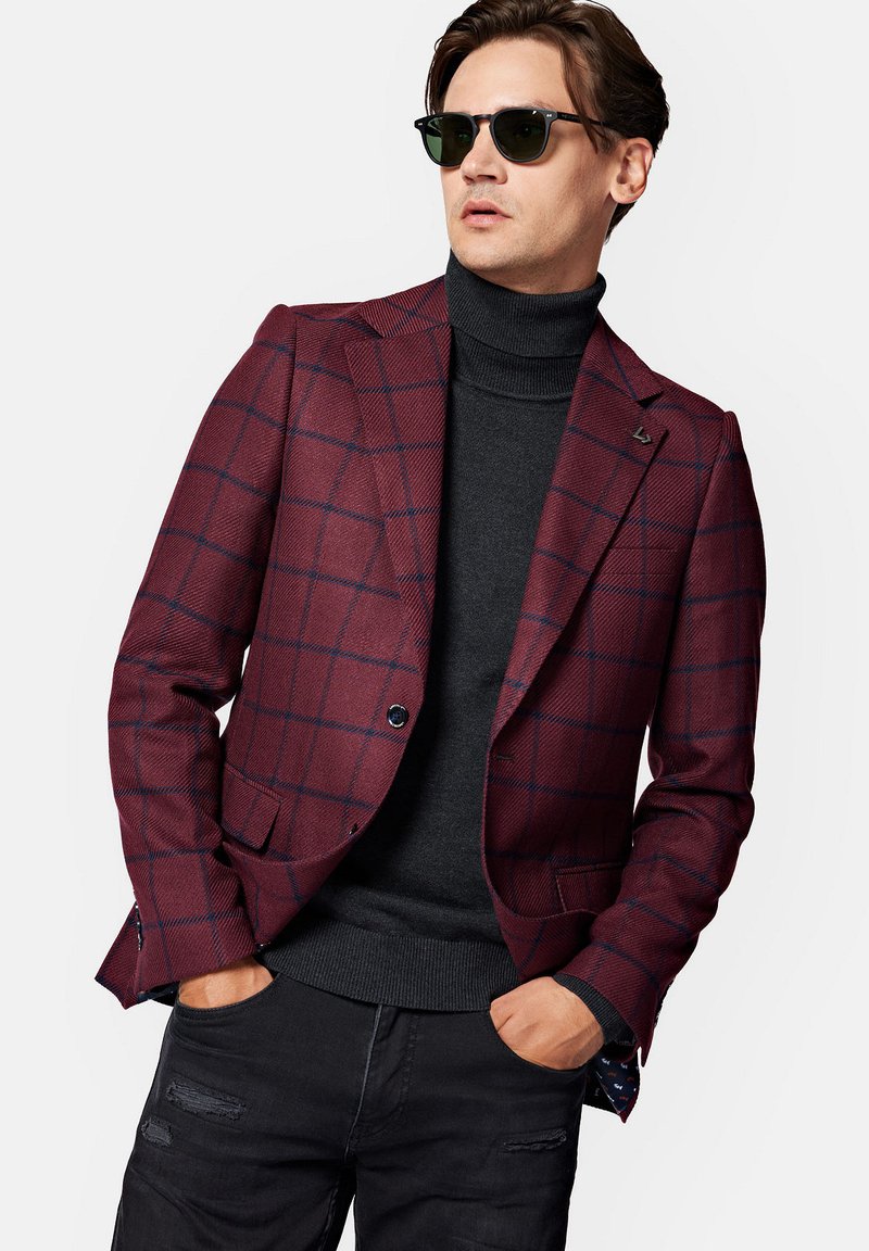 Burgundowa marynarka w kratę z teksturowanej tkaniny, z wyciętymi klapami, zapięciem na jeden guzik, noszona na czarnym golfie i czarnych przetartych dżinsach.