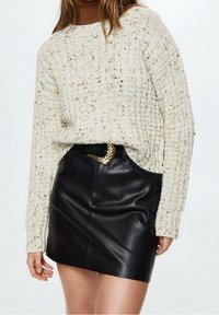 Cremfarbener, gerippter Strickpullover mit einem aufgerollten Kragen, kombiniert mit einem schwarzen, ledernen Minirock und einem goldenen Kettengürtel als Akzent.