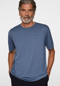 Herrblå kortärmad t-shirt tillverkad av ett mjukt, lätt tyg; har en rund hals och en liten logotyp på vänster bröst.