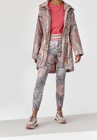 Lekka, wzorzysta kurtka przeciwdeszczowa z różowymi i liściastymi wzorami, zestawiona z różową bluzką oraz legginsami w liście. Uzupełniona wielokolorowymi trampkami.