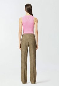 Top senza maniche rosa a coste con logo circolare sulla schiena, abbinato a pantaloni verde oliva a vita alta e gamba dritta con una finitura testurizzata.