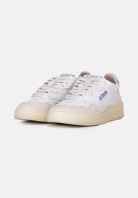 Sneaker in pelle bianca con accenti in suede beige chiaro, perforazioni testurizzate sulla punta e suole in gomma beige. Presenta lacci piatti e dettaglio del logo.