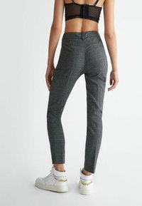 Rutet bukser i sort og hvidt stof, tætsiddende design, mellem høj talje, parret med hvide sneakers med højt skaft og kæde detaljer.