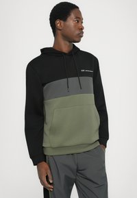 Sweat à capuche en noir, gris et vert olive. Tissu doux avec une poche avant, design coloré et logo sur la poitrine.