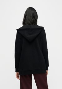 Black hooded sweatshirt with a relaxed fit, featuring a large hood, long sleeves, and ribbed cuffs. Soft fabric and minimal detailing.